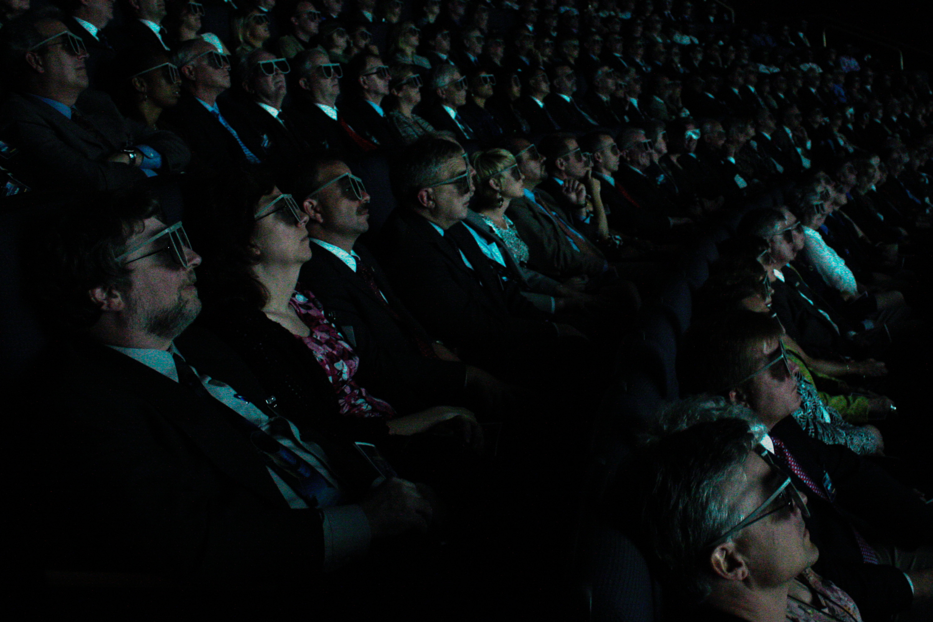 background image, a movie audience wearing 3-d glasses, all well dresssed and facing to the right